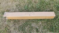 Long rectangular cardboard box with shipping label on grass background.