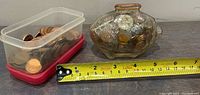 Glass piggy bank filled with pennies placed next to a container of pennies and a tape measure showing approximately 5.5 inches in length.