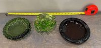 Three glass ashtrays placed side by side with a tape measure above them showing size, colors green and black visible.