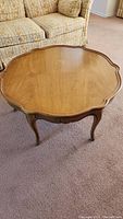 Full view of wooden coffee table with scalloped pie crust edge top and cabriole legs placed on carpeted floor.
