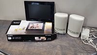 Sony digital photo frame with box, two Koss white speakers and power adapter on wooden surface