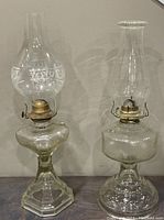 Two vintage glass oil lamps side by side against a neutral background showing overall height and condition.