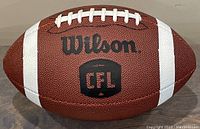 Side view showing Wilson branding along with the CFL logo on brown leather surface with white stripes