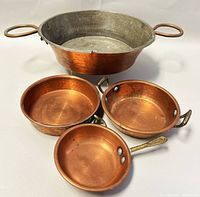 Top view of four copper and metal pots arranged in a group showing interiors and handles.