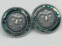 Front view of the pair of circular Haida Indigenous earrings made of pewter and mother of pearl with intricate traditional face designs and mother of pearl inlays.
