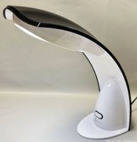 Front-side view of the OttLite GX8026 desk lamp showing the sleek curved profile, black and white color, and on/off switch on base.