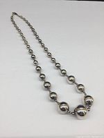 Full view of the sterling silver graduated ball necklace laid flat on a white surface showing the variation in bead sizes along the chain.