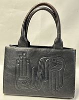 Front view showing embossed Haida art hands design on black leather purse with rounded handles.