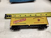 Close-up of the Budweiser beer train car model on white surface with measuring tape showing length approximately 7 inches.