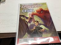 Photo of The Amazing Spider-Man #1.2 comic book showing the front cover with Spider-Man illustration and part of the storyline title 'Above the Crawl'.