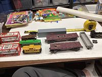 Total lot overview showing various train cars and parts on a table, including flatcars, passenger and freight cars, and measuring tape for scale.