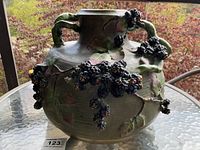 Front and side view of large green ceramic amphora vase with clusters of realistic blackberries and twisting green vines and leaves in relief on the surface.