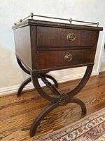 Front view of mahogany side table showing crossed leg base, two drawers with brass ring pulls, and metal gallery around top
