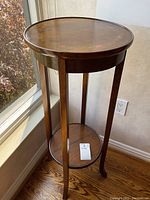 Full view of the antique walnut pedestal table showing round top, long legs and lower shelf.