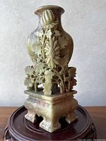 Front view of a carved soapstone vase with raised floral patterns on a rosewood stand.
