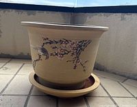 Side view of cream pottery planter showing floral and bird painted decoration and attached saucer.