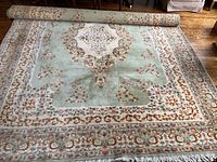 Overall view of pale green carpet partially rolled showing full design and size