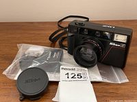 Nikon L35AF camera with lens cap and instruction manual in plastic bag on wooden surface