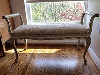 Full front view of bench by window showing overall shape, scrolled arms, cabriole legs and upholstered seat