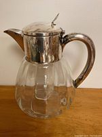Front and side view of the glass water pitcher with silver plated handle, lid and spout. Visible internal ice tube for cooling.