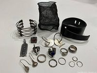Photo of the entire jewelry lot featuring rings, bracelets, earrings, a pendant, and a leather cuff bracelet all arranged on a white surface.