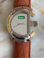 Close-up of round silver-tone case, gold-tone Bossini bezel and white dial with green logo