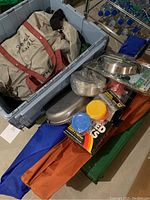 Closed grey storage container with multiple camping items including duffel bag, pots, and folded tents or poles.