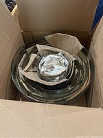 Set of 7 glass mixing bowls nested inside an open cardboard box with protective paper packing inside. Bowls are clear and appear unused.
