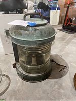 Multiple views of a vintage heavy-duty nautical lantern with a patina finish and a large fishbowl style glass lens. Untested condition with rust on some metal parts.
