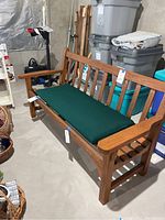 Side-angle photo showing the bench with green cushion, wood slat back, and armrests in storage room.