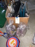 Box containing folded metal and fabric camping chairs, two teal cushioned stadium seats, plastic cups sealed in plastic bag, disposable plates.