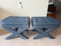 Front view of two blue upholstered seats/ottomans with polka dot fabric and tufted cushions on X-leg bases.