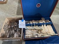 Silverware chest with vintage silver plated silverware, some wrapped in paper, showing blue lining and compartment layout