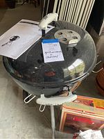 Weber charcoal grill closed with instruction manual and boxed accessories visible next to it.