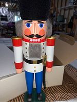 Wooden nutcracker figure painted with white, red, blue, and gold colors, with gray hair and beard, standing upright on a table.