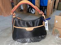 Photo showing shoulder tote style bag with black textured material, tan leather strip with brand embossing, and part of blue ribbon tied to tag