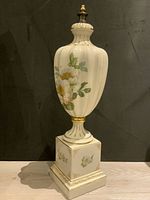 Front angle view of tall porcelain vessel with floral design and gold accents on pedestal base.
