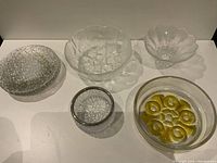 Six Scandinavian glass pieces on white background showing variety of bowls and plates with different textures and colors including yellow accents and smoke-colored sections.