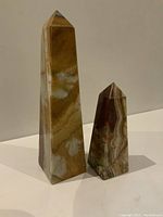 Photo showing front view of two onyx obelisks, taller with brown cream veining and smaller with burgundy green hues.