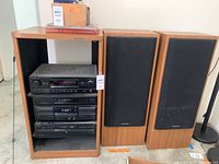 Wood grain stereo cabinet housing Kenwood components and two speakers on either side. Identifies overall lot layout and condition.