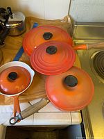 Three orange enameled cast iron pots with lids on a countertop near stove
