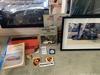 Photo showing framed Porsche photograph, Porsche books, pins, patch badges and a Porsche 911 GT2 model.