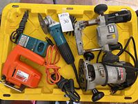 Photo showing the full lot of power tools on a yellow plastic surface including Black & Decker jig saw, Makita grinder, Porter Cable routers