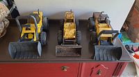 Set of three metal Tonka tractors lined up side by side showing front scoops and wheels.