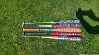 Full view of all five baseball bats laid on grass showing the designs and grips clearly.