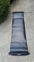 Full view of the black slide board mat laid out on the ground showing its length and material texture.