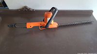 Full view of the Black & Decker electric hedge trimmer showing the orange body, black handle, and cutting blade.