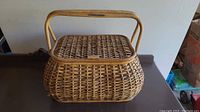 Photo of large wicker picnic basket showing front angled view with handle upright and lid closed.