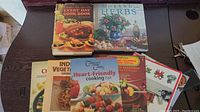 Photo showing six assorted cookbooks arranged on a wooden surface, titles clearly visible.