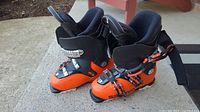 Pair of orange and black Salomon ski boots photographed from the side on a concrete surface outdoors.